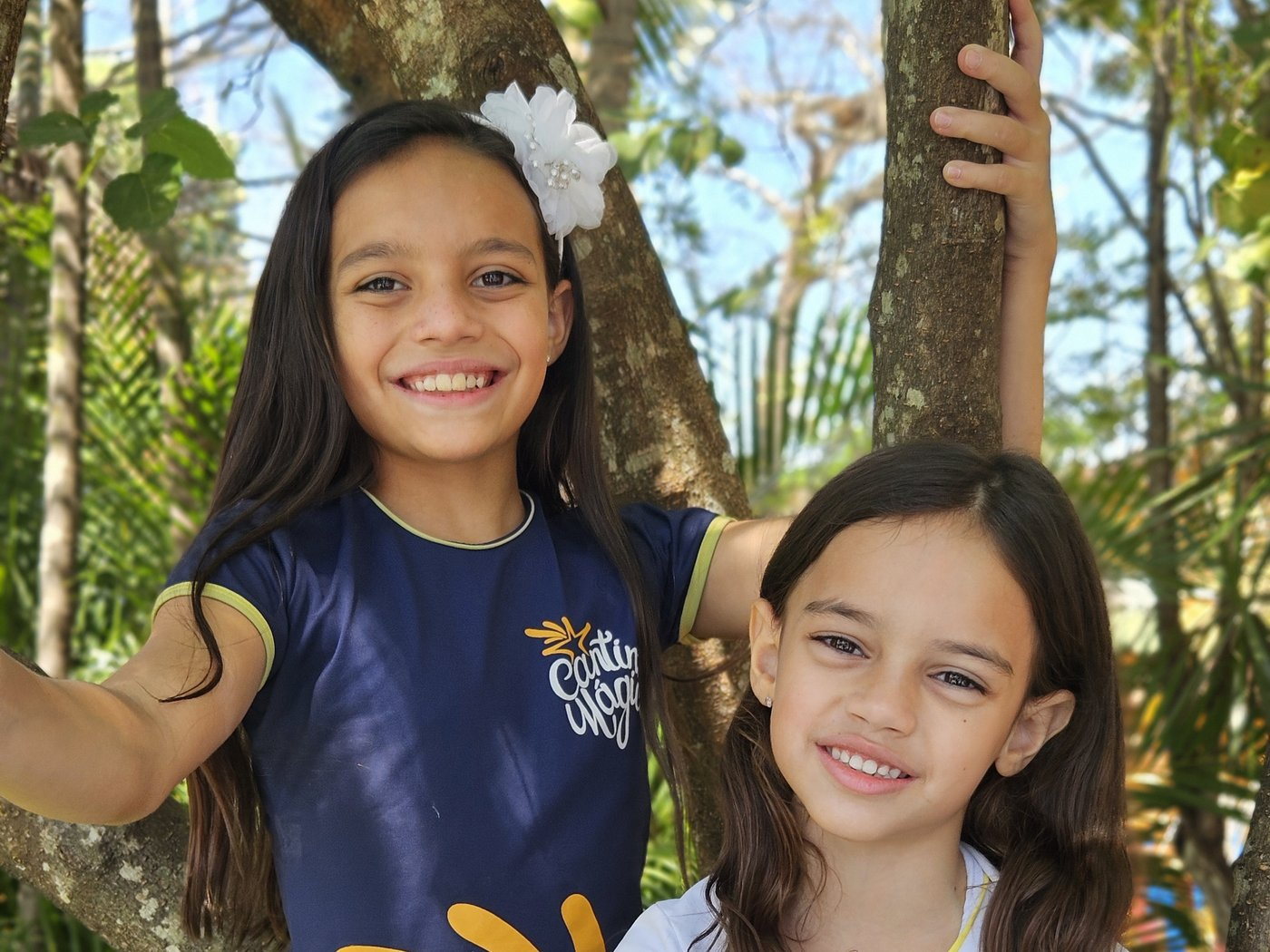 Duas alunas do Cantinho Mágico sorrindo no jardim da escola, entre as árvores